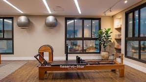 Quarto moderno com um aparelho de Pilates reformer, grandes janelas e uma planta.