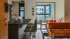 Uma cozinha moderna com área de bar, mesa de jantar com cadeiras e vista para um edifício pela janela.