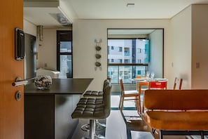A modern kitchen with a bar area, a dining table with chairs, and a view of a building through the window. - Club Vista Mar Pertinho do Beto Carrero (Penha)