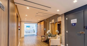 A hotel corridor with a reception desk, seating area, and lockers.