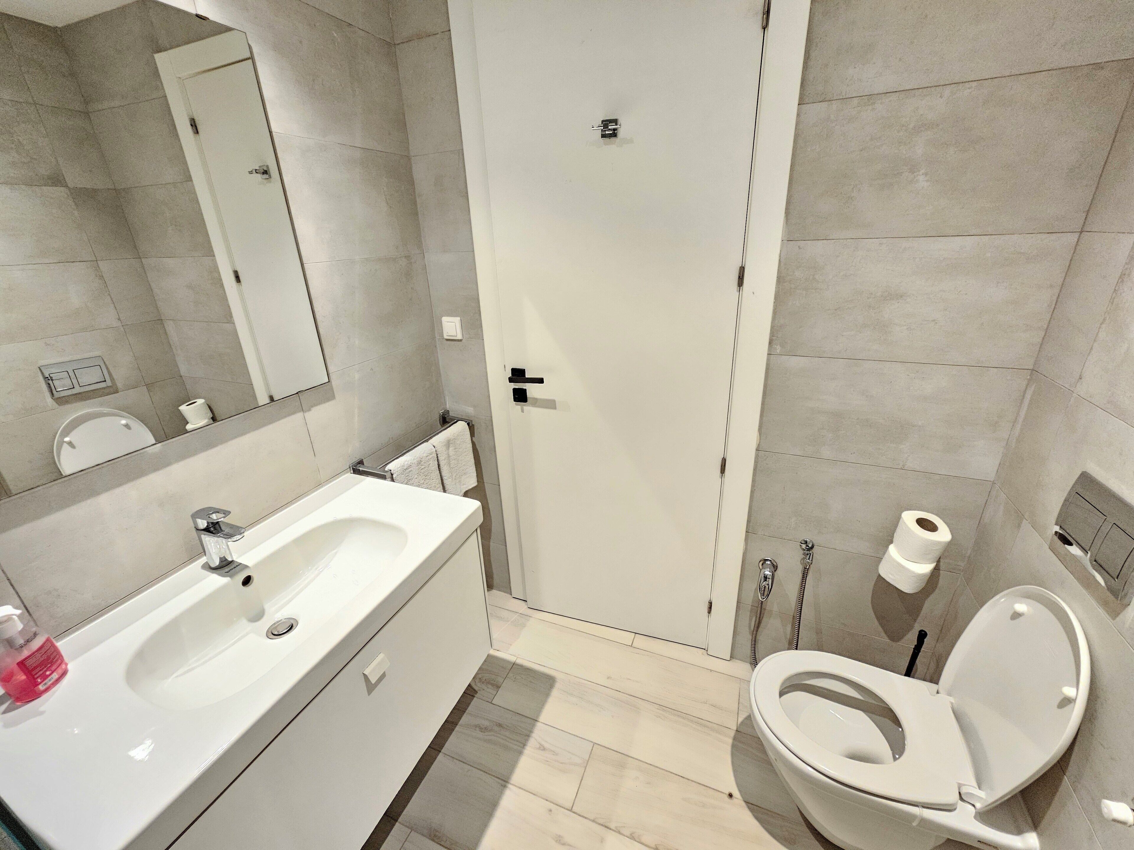 Ein modernes Badezimmer mit Waschbecken, Toilette und Duschbereich in Weiß.