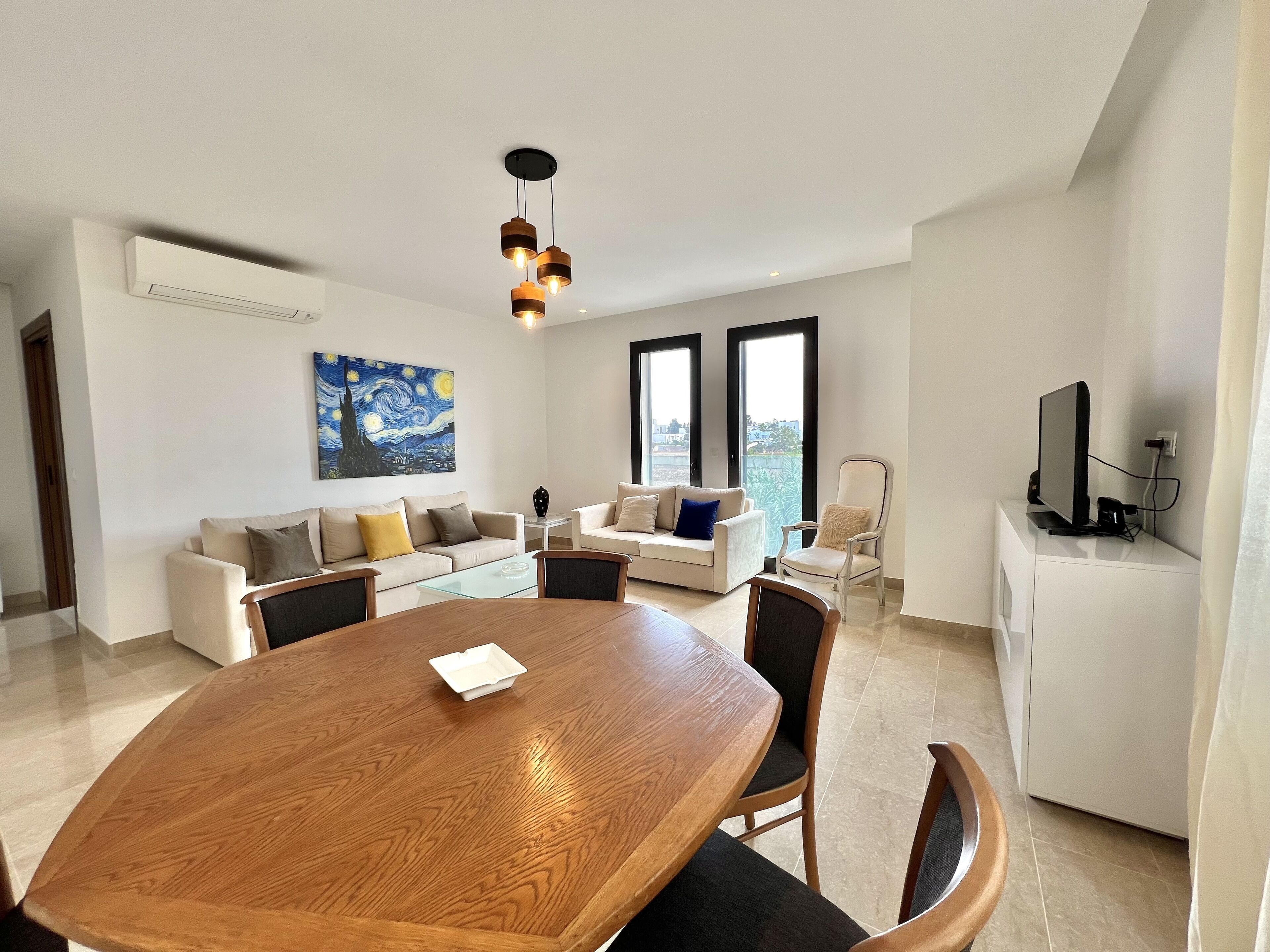 Una sala de estar moderna con una mesa redonda de madera, dos sofás, un televisor y un cuadro en la pared.