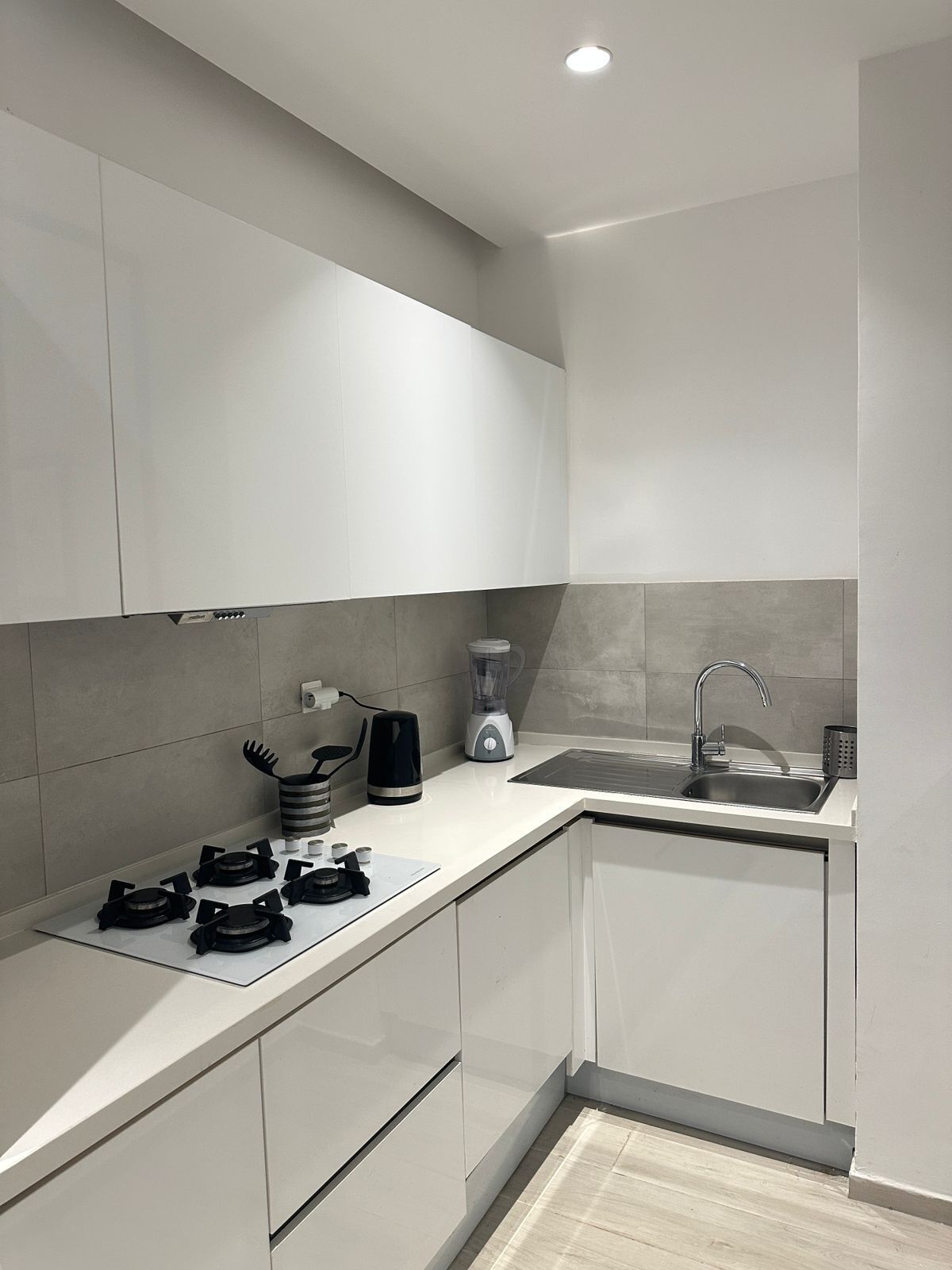 A modern kitchen with white cabinets, a built-in stove, a sink, and a blender.