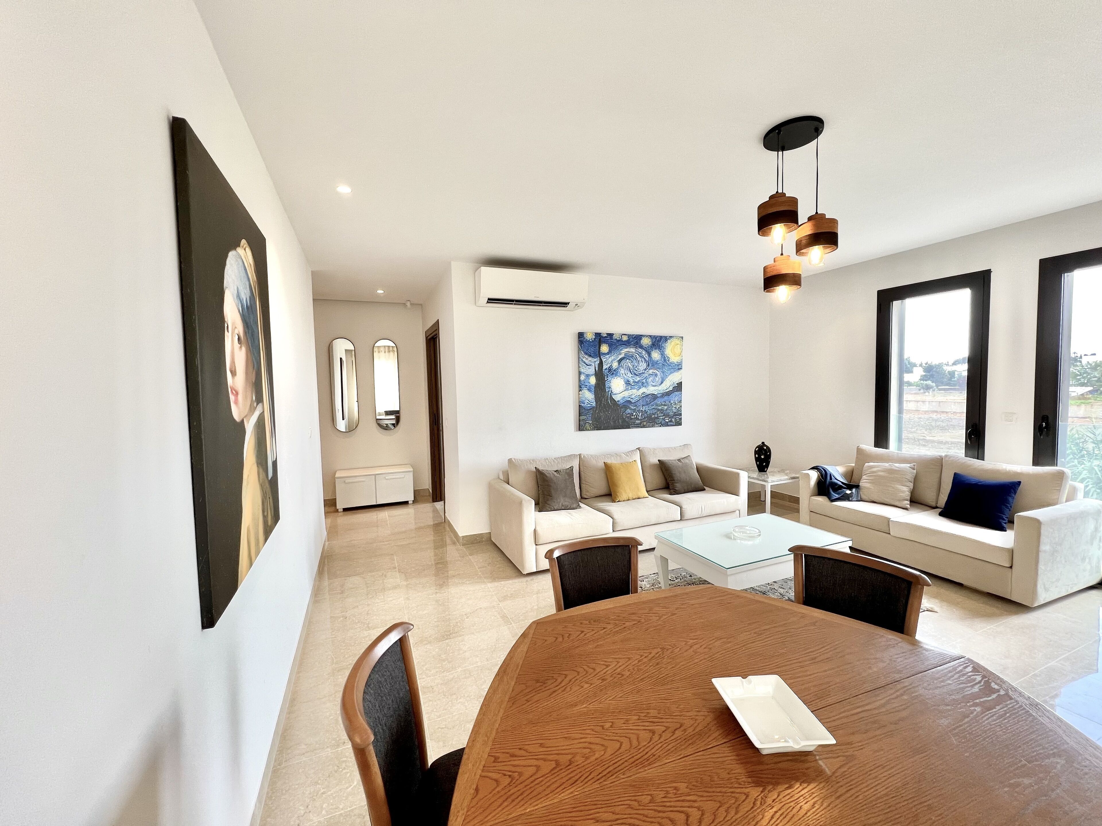 A modern living room with a dining table, sofas, and artwork on the walls.