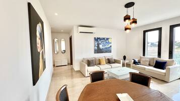 A modern living room with a dining table, sofas, and artwork on the walls.