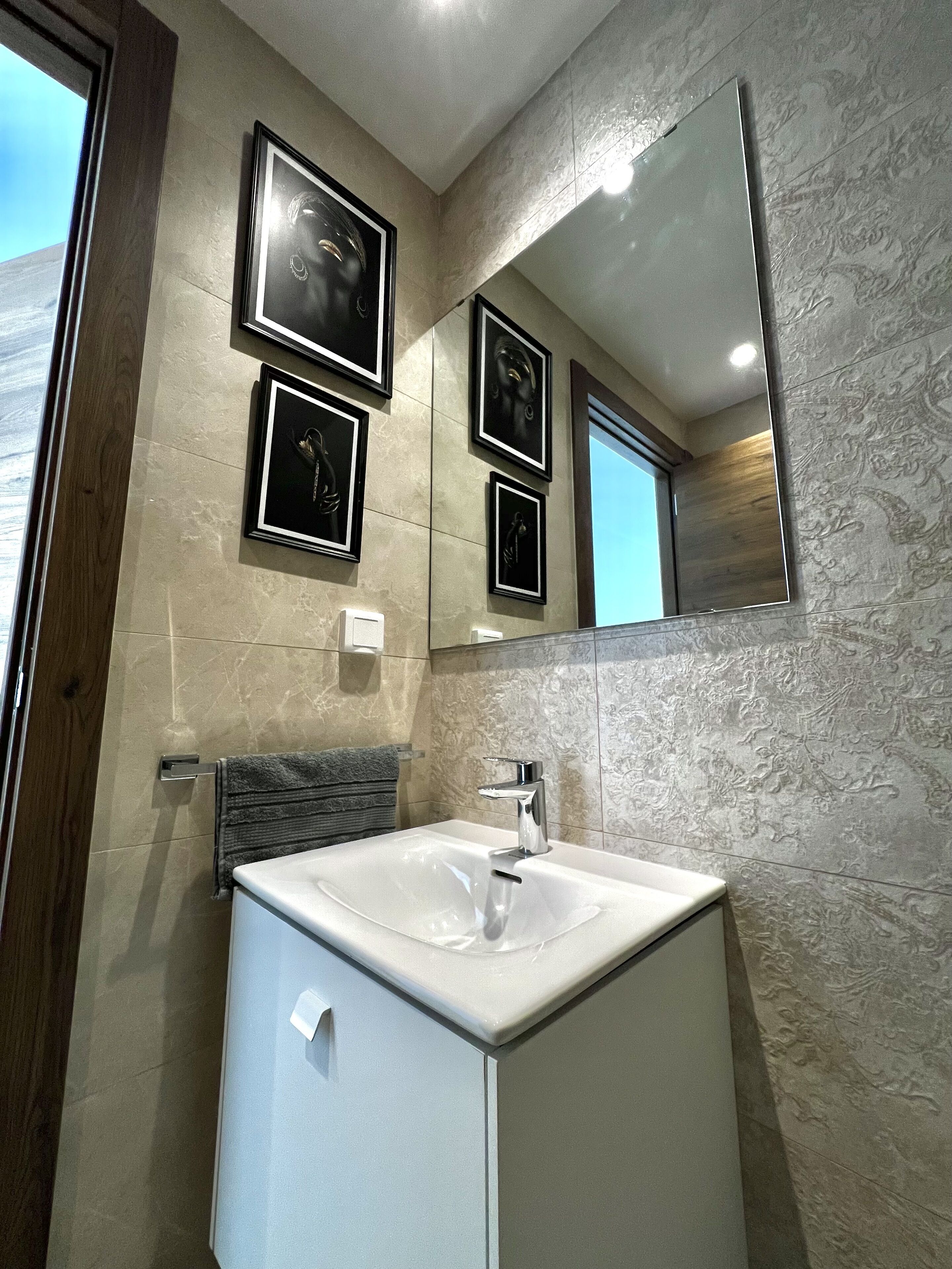 Un baño moderno con un lavamanos blanco, un espejo y obras de arte enmarcadas en la pared.