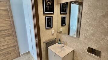 A modern bathroom with a white sink, mirror, and toilet. There are framed pictures on the wall and a wooden door.
