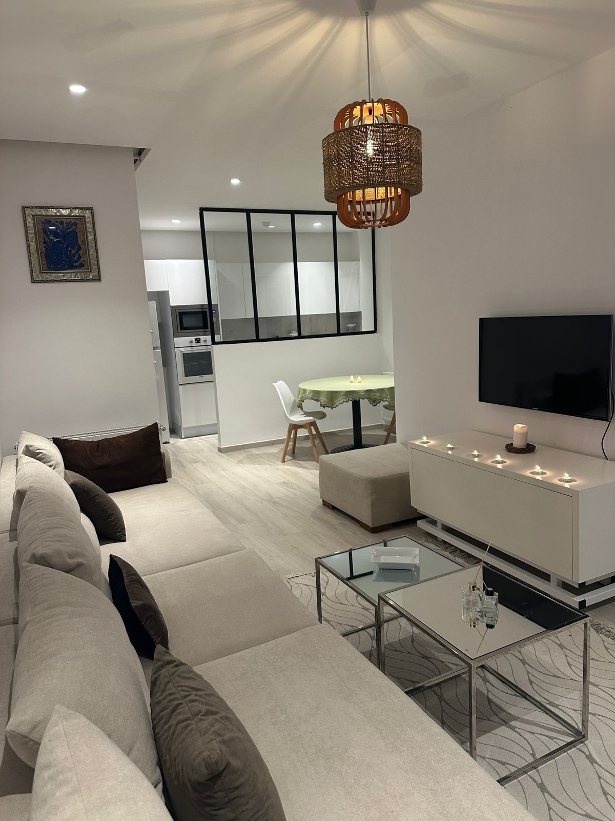 Een moderne woonkamer met een bank, een glazen salontafel en een televisie. In de achtergrond bevindt zich een eethoek met een tafel en stoelen.