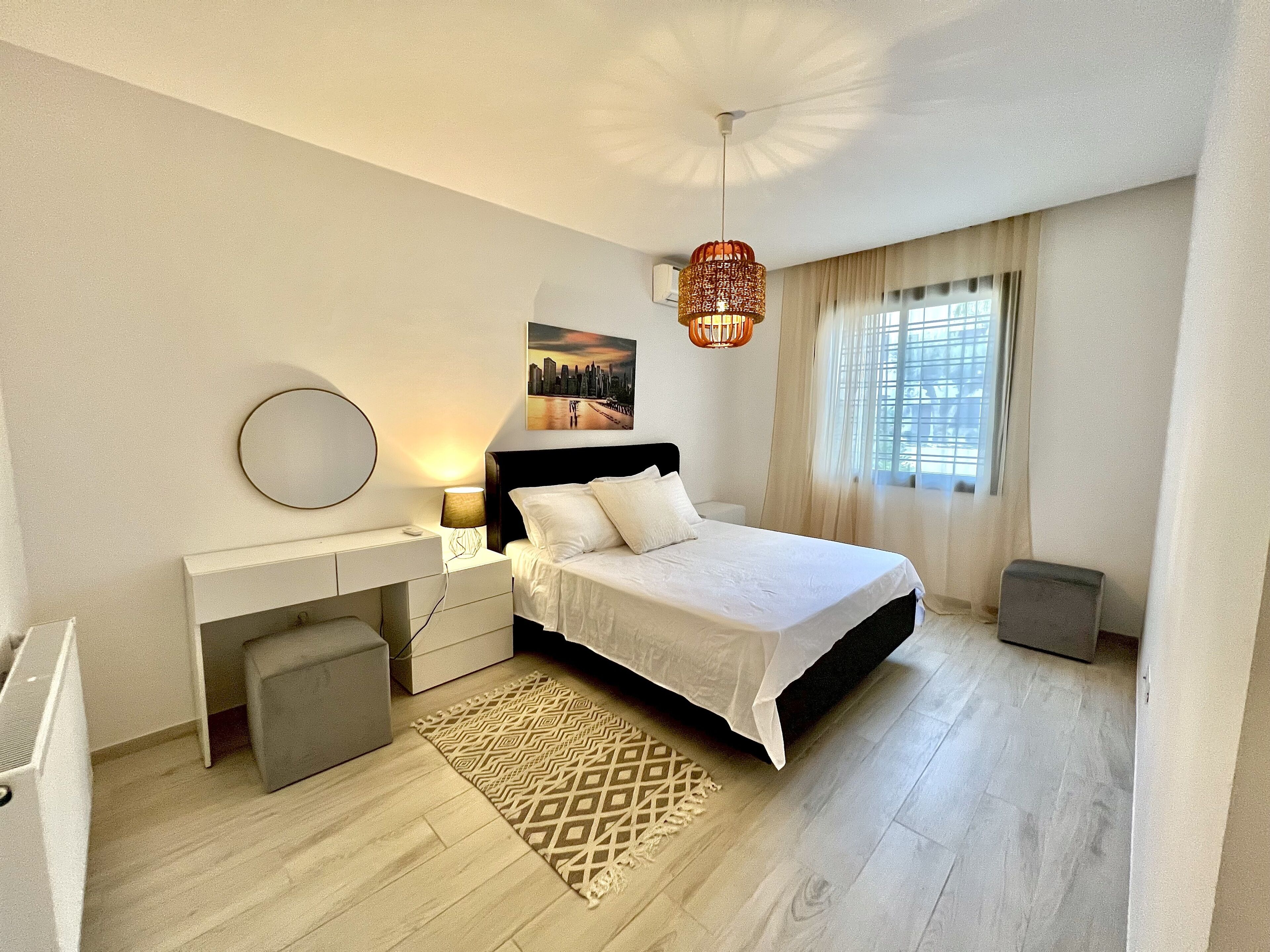 A bedroom with a bed, bedside table, lamp, and a cityscape painting on the wall.