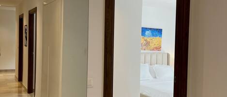 A hotel hallway with a bed in the background, a painting on the wall, and a wooden door frame.