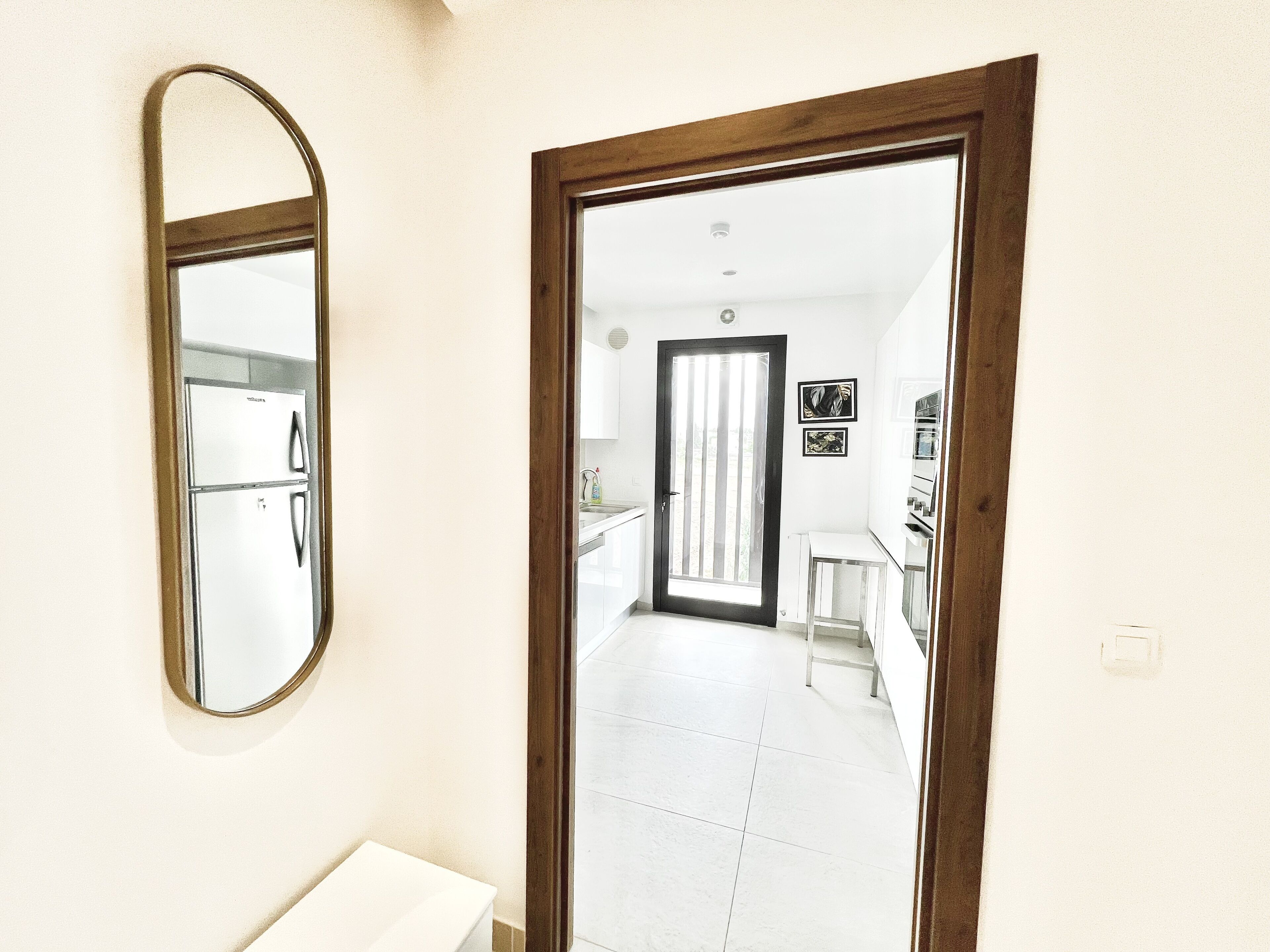 Un pasillo que conduce a una cocina con refrigerador, pileta y puerta con vista al exterior.