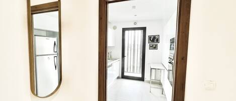 Un pasillo que conduce a una cocina con refrigerador, pileta y puerta con vista al exterior.