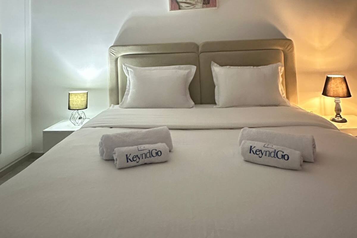 Ein Hotelzimmer mit einem Bett, zwei Kissen, einem Kopfteil, einem Bild an der Wand und zwei Nachttischlampen.