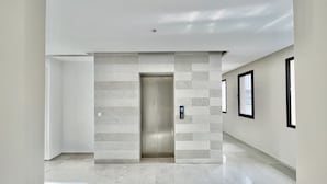Een moderne hal met een metalen lift, lichte wanden en een betegelde vloer.