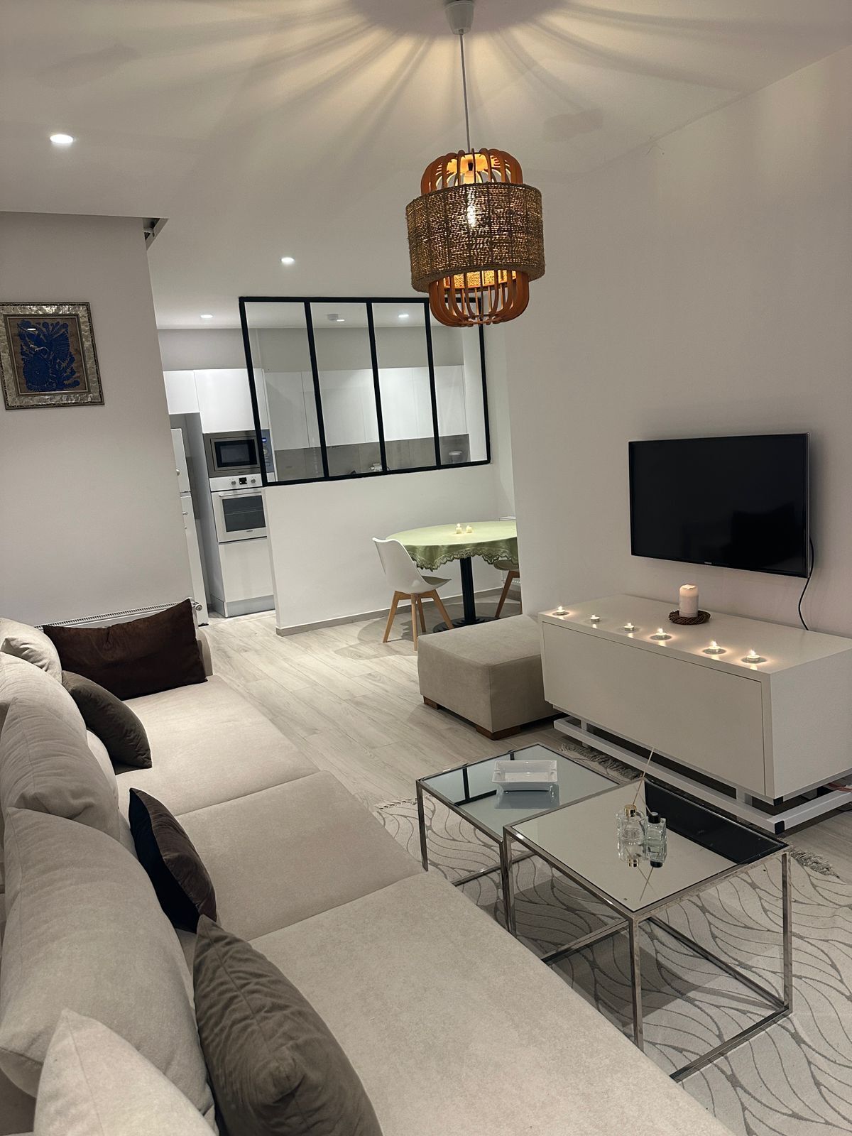En moderne stue med sofa, sofabord i glas, et fladskærms-tv og et spiseområde med bord og stole.