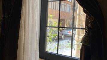 A window with a view of a street, curtains partially drawn, and a glimpse of a building outside.