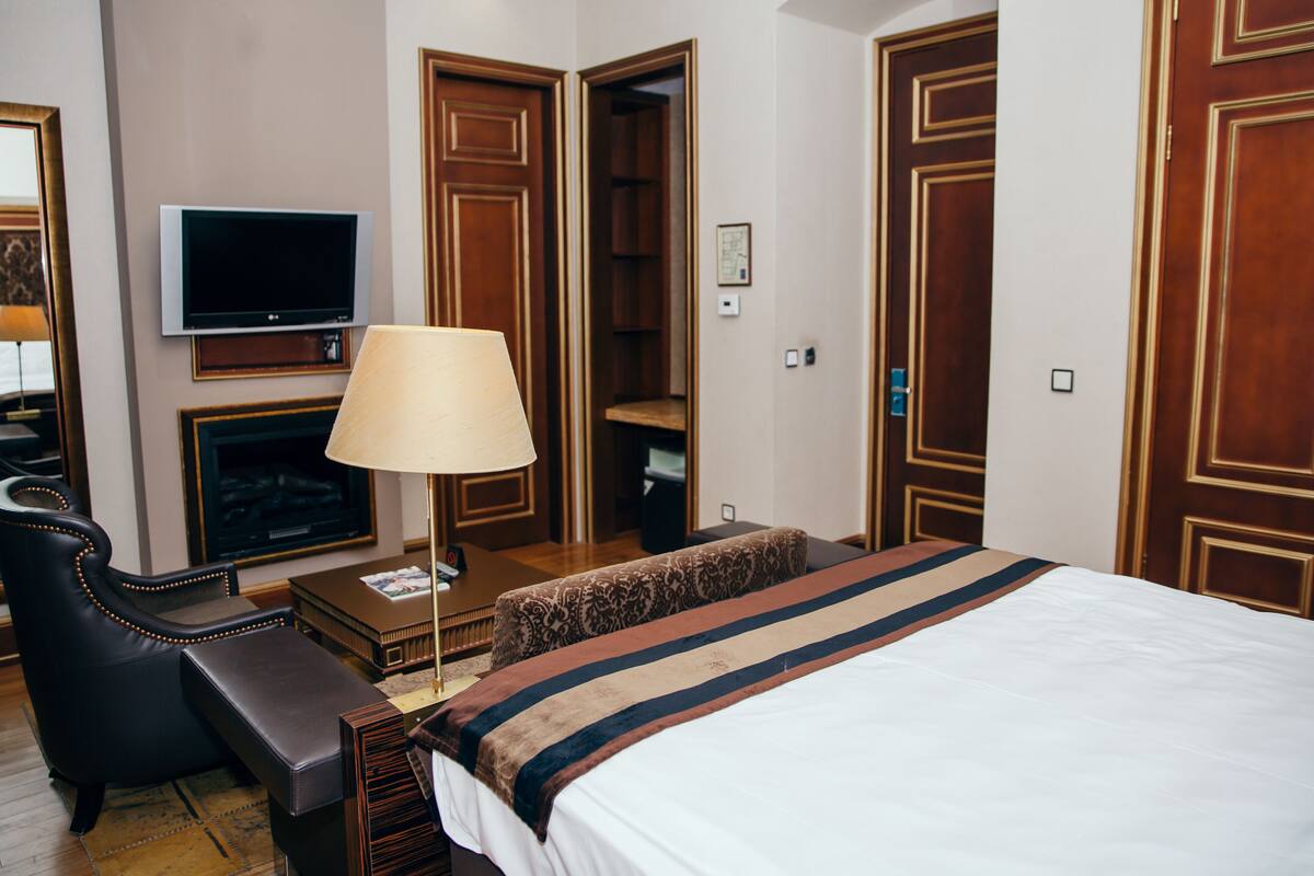 A hotel room with a bed, a TV, a desk, a lamp, a chair, and a closet.