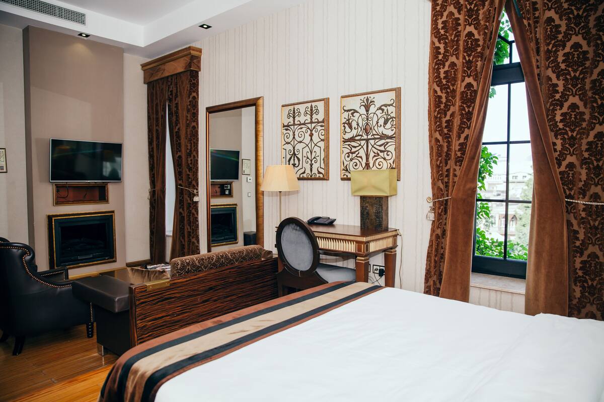 A hotel room with a large bed, a desk, a chair, a television, and a window with curtains.