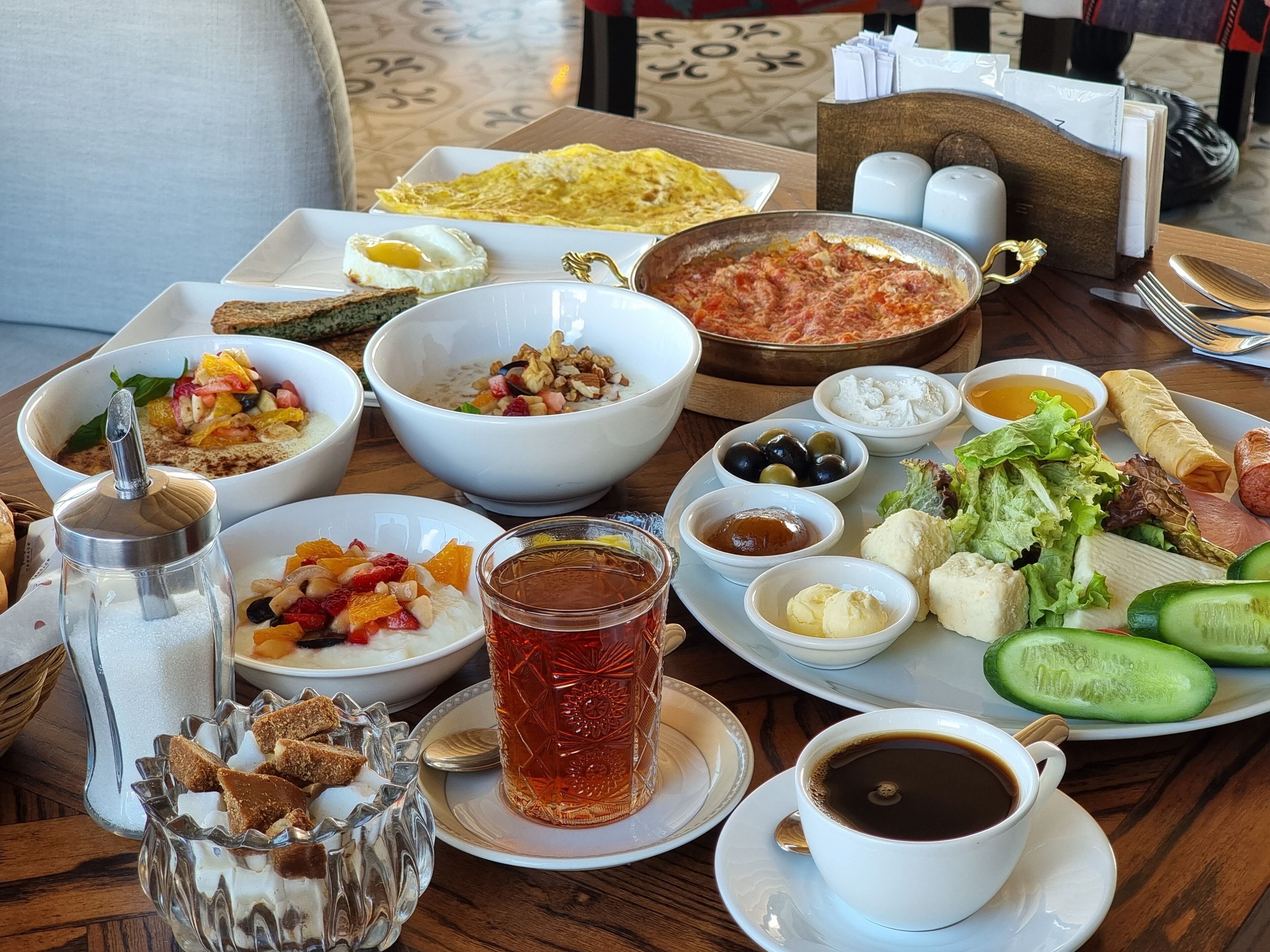 A breakfast spread with various dishes, including eggs, bread, and vegetables, on a wooden table.