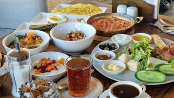 A breakfast spread with various dishes, including eggs, bread, and vegetables, on a wooden table.