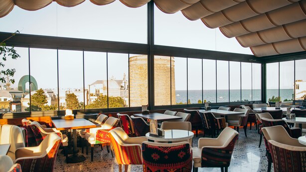 Un restaurante con terraza y vistas al mar, con mesas y sillas de tapicería estampada.