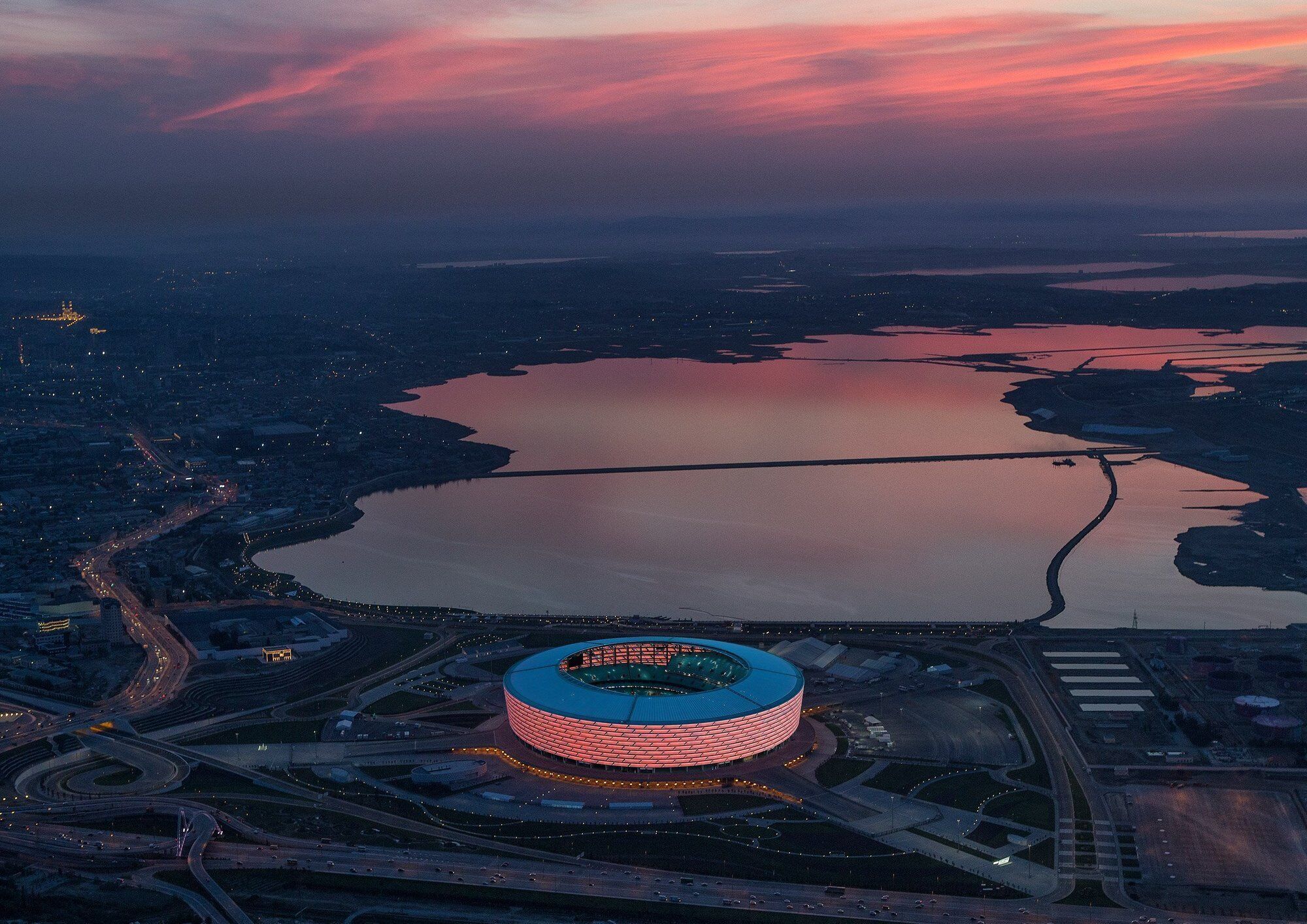 Vista aerea di uno stadio dalla forma circolare, circondato da strade e da una distesa d'acqua.