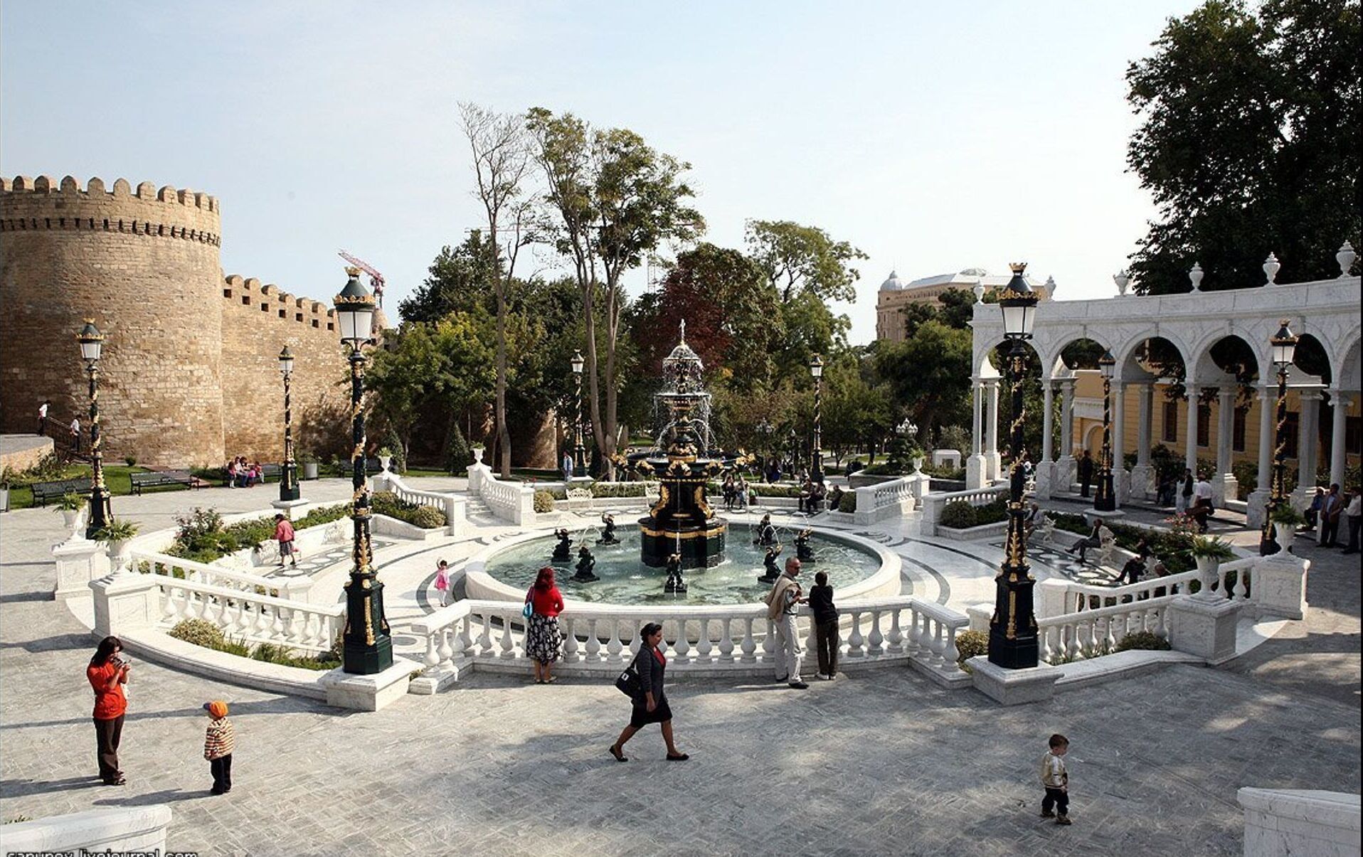 Ett historiskt torg med en central fontän, en slottsmur och en klassisk byggnad med valv.