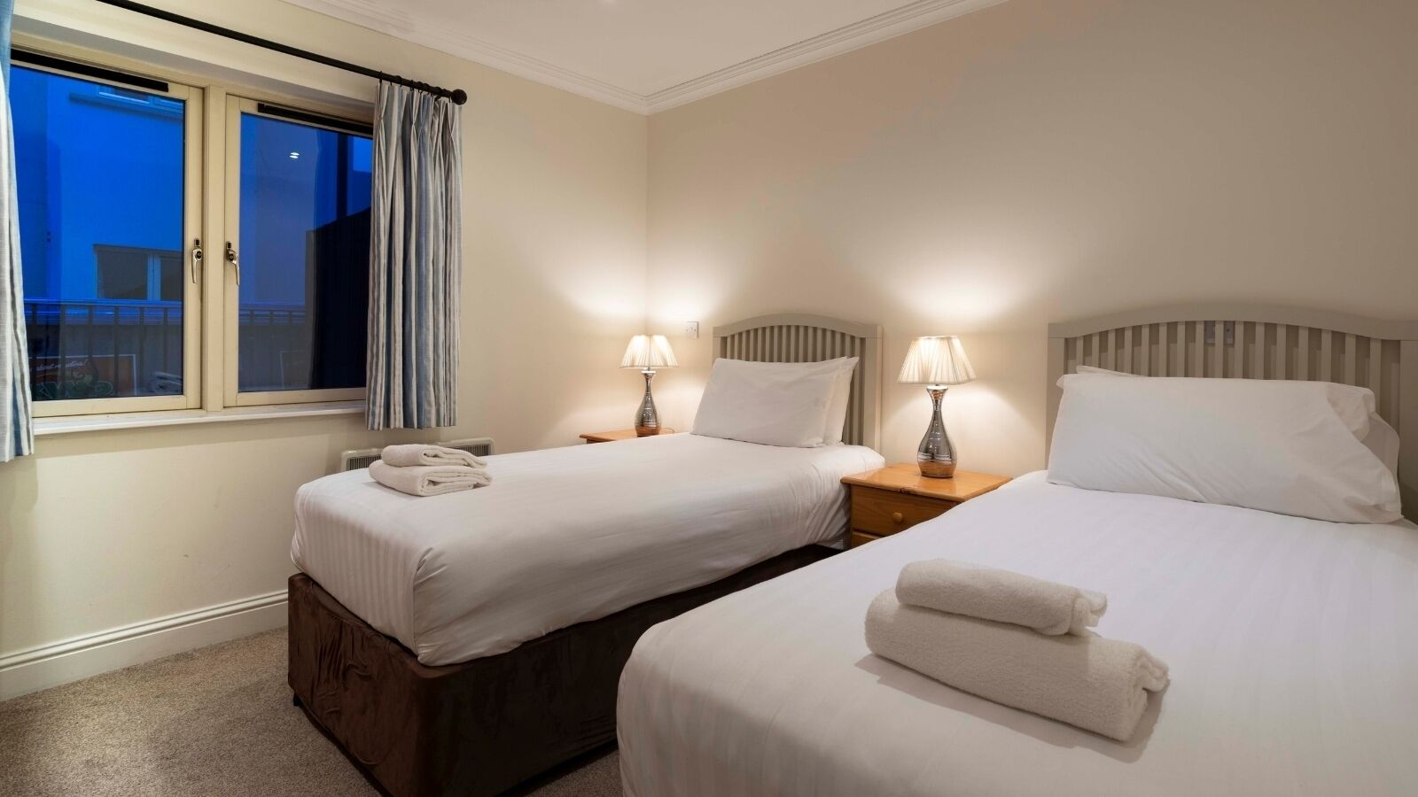 Ein Hotelzimmer mit zwei Betten, einem Fenster mit Vorhängen, Nachttischlampen und Blick nach draußen.