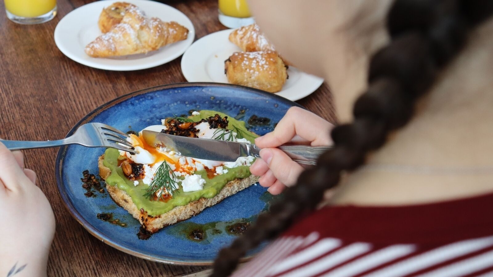 A person eating a slice of pizza with toppings on a blue plate.