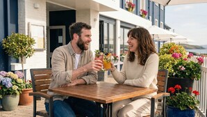 Una pareja sentada en una mesa de madera, rodeada de macetas con plantas y flores.