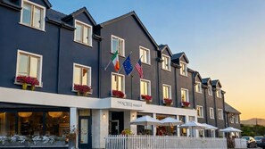 A hotel with multiple stories, balconies with flowers, and flags of Ireland and the EU. - Schull Harbour Hotel (Schull)
