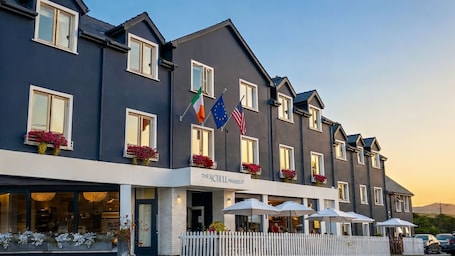 A hotel with multiple stories, balconies with flowers, and flags of Ireland and the EU.