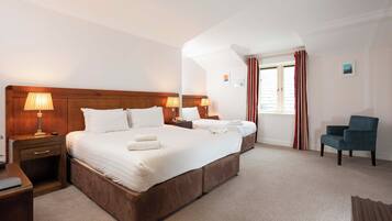 A hotel room with a large bed, two bedside tables with lamps, a chair, and a window with curtains.