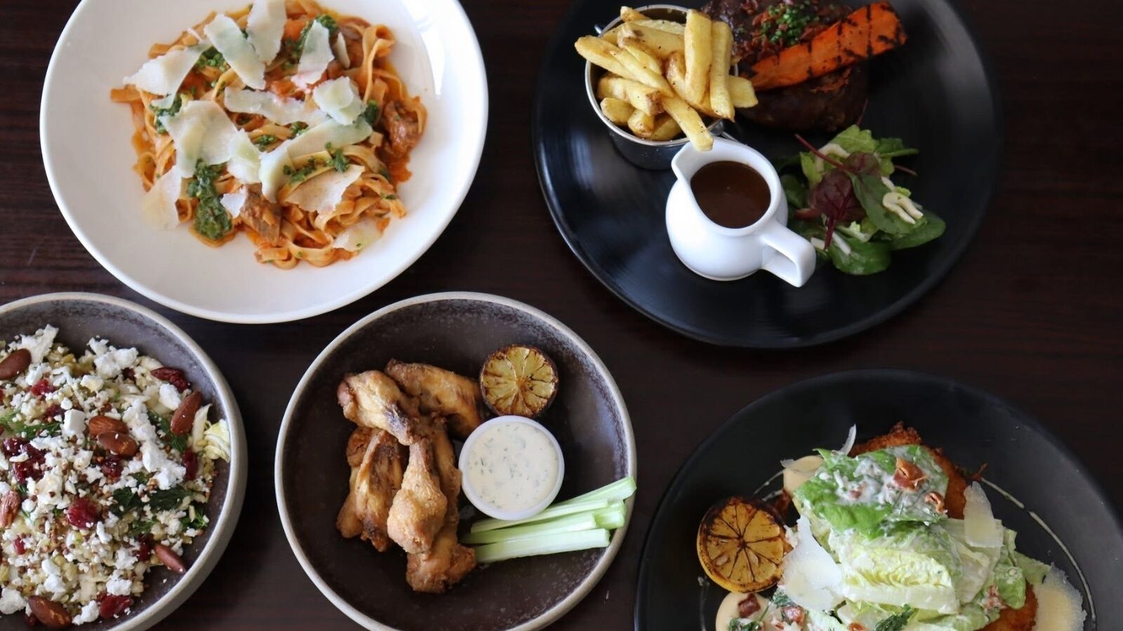 Een tafel met verschillende gerechten, zoals pasta, friet, kippenvleugels en salades.