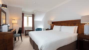 Habitación de hotel con una cama grande, un escritorio con silla, una lámpara y un ventanal con cortinas.