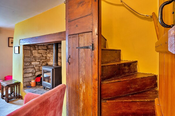 A wooden staircase leading to a second floor, a stone fireplace, and a small table with a red chair in a room with yellow walls.