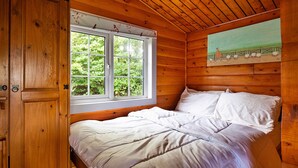 A wooden cabin room with a bed, a window with blinds, and a painting on the wall. - Mountain View (Trawsfynydd)