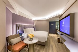 A hotel room with a bed, a desk with a chair, a TV mounted on the wall, and a small table with a vase of flowers. - Manxin Hotel Zhangjiagang Jingang Avenue Pedesrian (Suzhou)