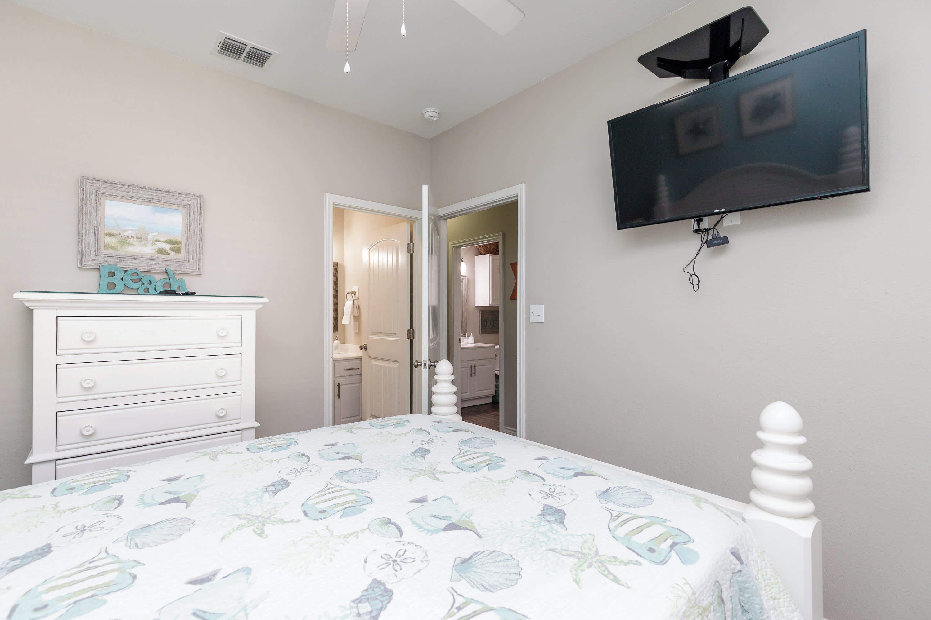 Quarto com cama, penteadeira e televisão na parede.
