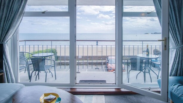 Habitación con balcón que da a una playa, con una mesa y sillas, y vista al mar.