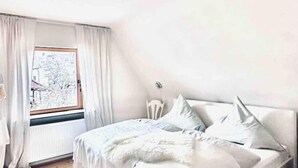 A bedroom with a bed, a window with curtains, a radiator, and a chair. - Galeriewohnung mit Ambiente (Wertheim)