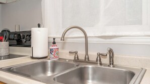 Une cuisine équipée de deux éviers en acier inoxydable, d’une cuisinière et d’une fenêtre agrémentée de rideaux blancs.