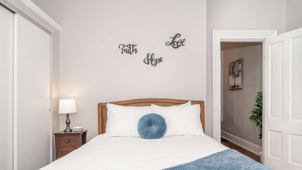 Une chambre à coucher avec un lit, une table de chevet, une lampe et un mur sur lequel sont inscrits les mots « Foi, Amour, Espoir ».