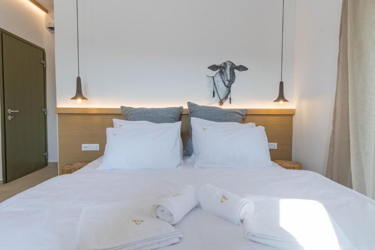 Cama bem arrumada com roupas de cama e toalhas brancas, cabeceira de madeira e duas luzes pendentes.