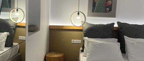 Un dormitorio moderno con una cama, un espejo redondo, un taburete de madera y un cuadro enmarcado en la pared.