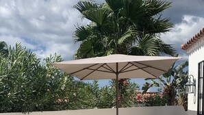 Un área junto a la piscina con dos sillones, una planta en maceta y una piscina con baldosas.