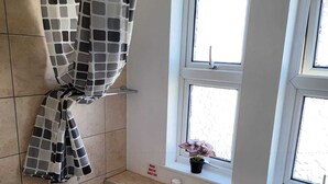 Un baño con bañera, inodoro, lavabo y una ventana en lo alto, además de cortina de ducha.