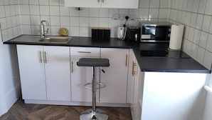 Una cocina compacta con armarios blancos, una encimera negra y un suelo de madera con patrón de espiga.