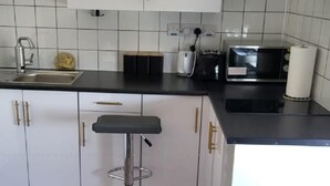 Una cocina con armarios blancos, encimera negra, un lavamanos, un tostador y un taburete de bar.