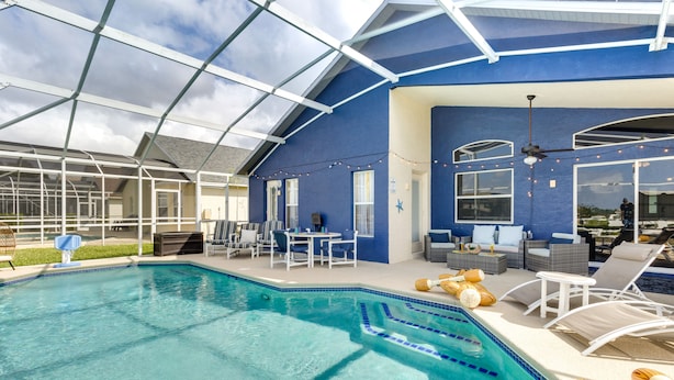 A pool area with a glass enclosure, lounge chairs, and outdoor seating. - Davenport Home w/ Game Room, Home Theater, Pool (Davenport)